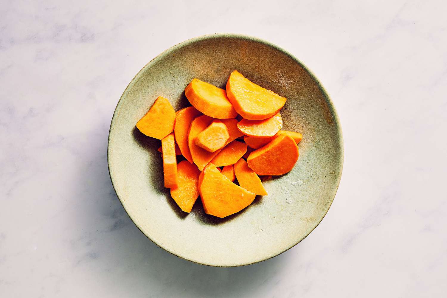 A bowl of sliced sweet potato tossed in oil and seasoned with salt