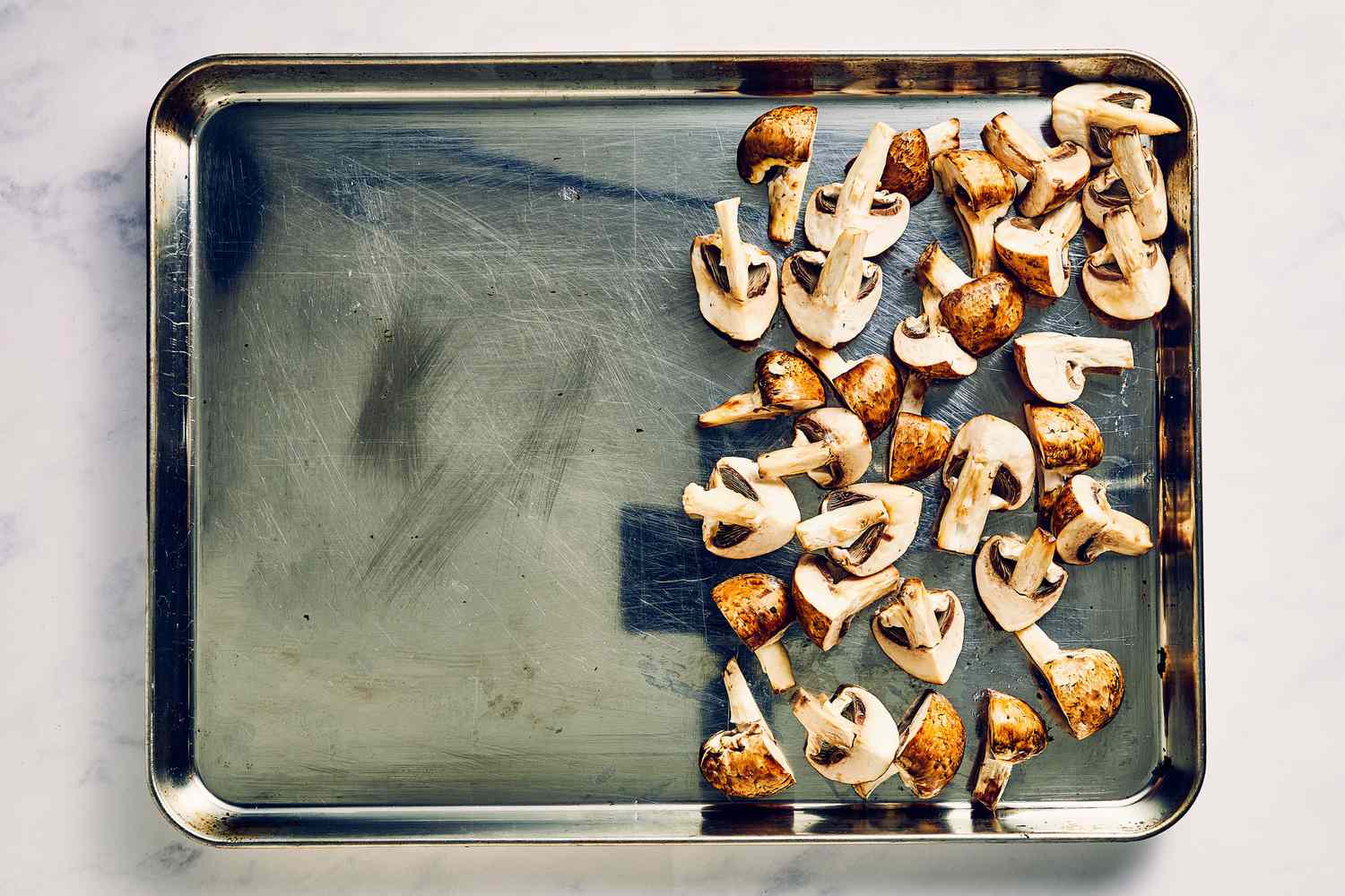A sheet pan with half the pan covered in cremini mushrooms tossed in oil and seasoned with salt