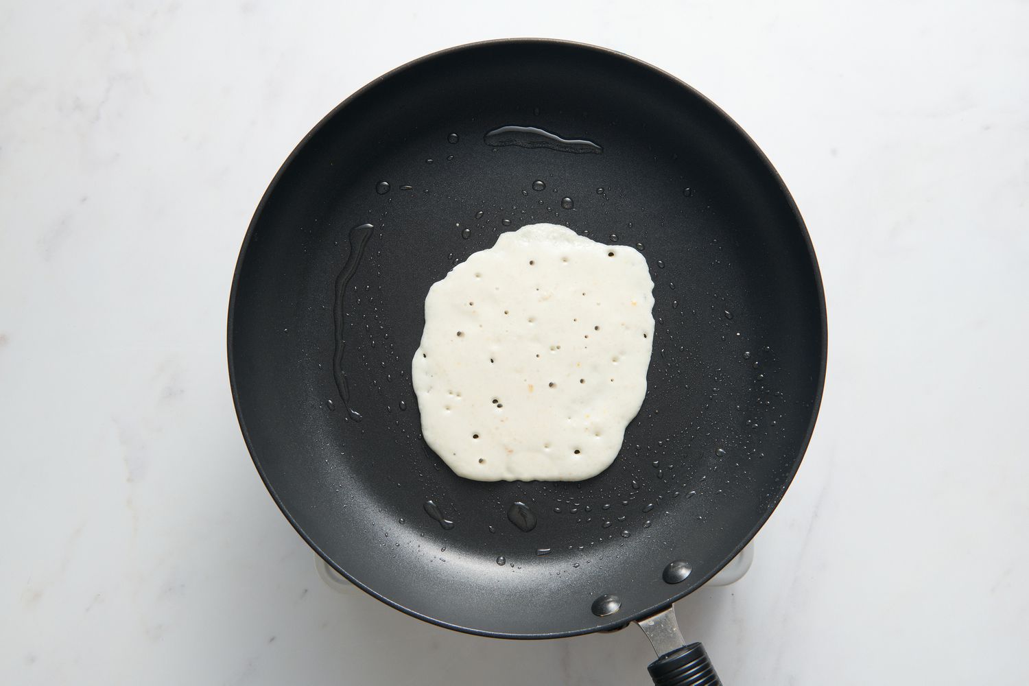 A small portion of the batter poured into the middle of the greased nonstick pan