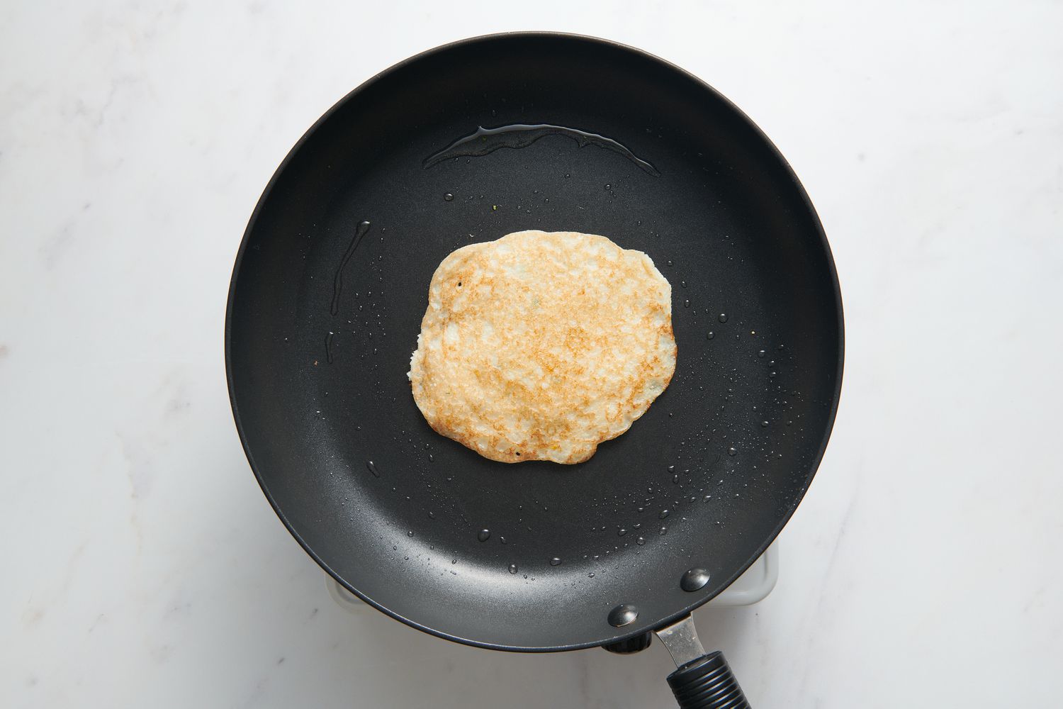 A greased skillet with a browned Uttapam in the center, onion-chile-cilantro side face down
