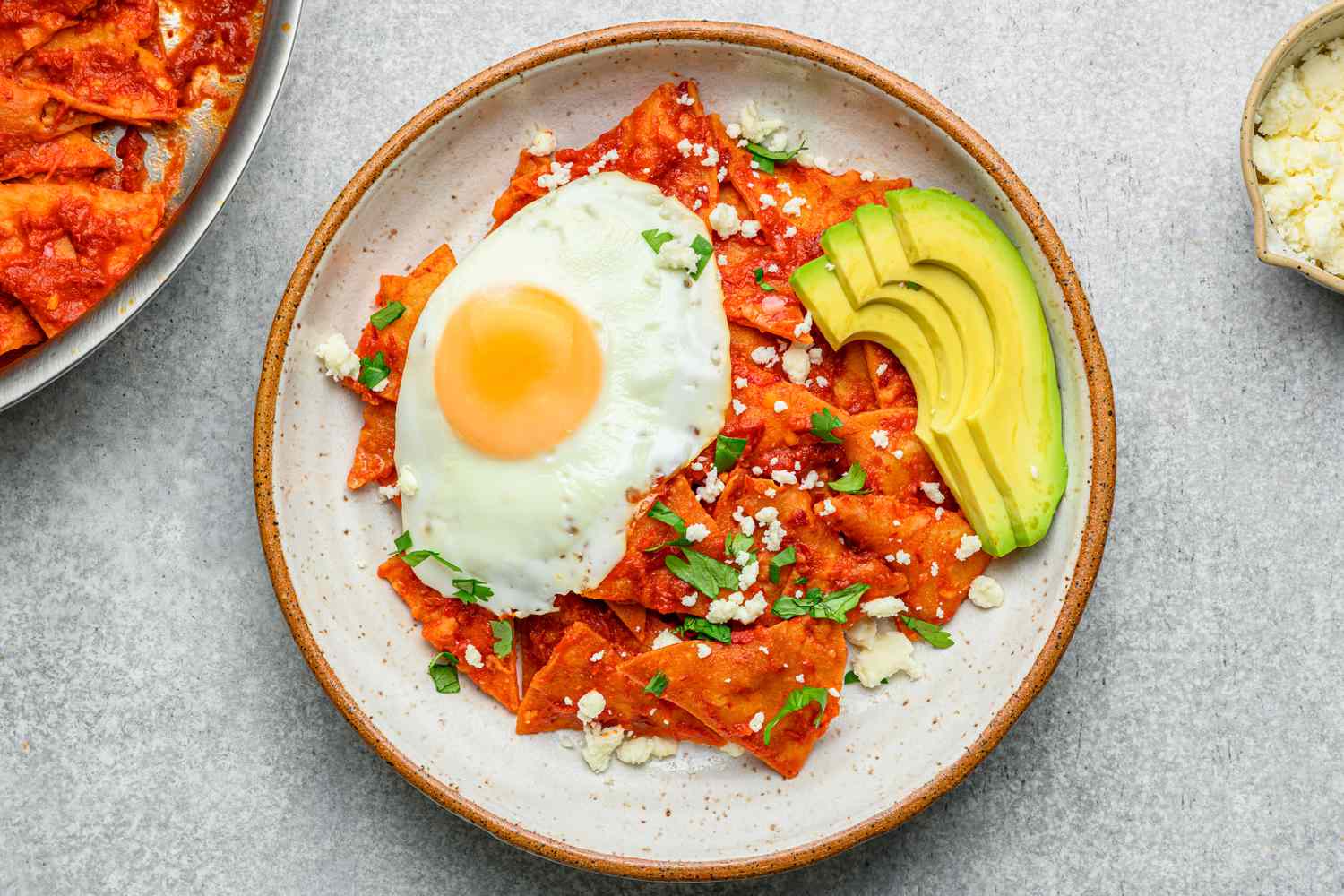 A plate of chilaquiles topped with a fried egg, cilantro, queso fresco, and sliced avocado