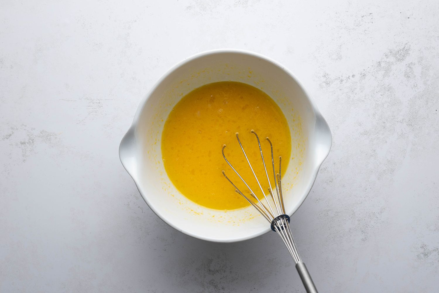 Eggs, yolks, sugar, lemon zest and juice mixture in a bowl with a whisk