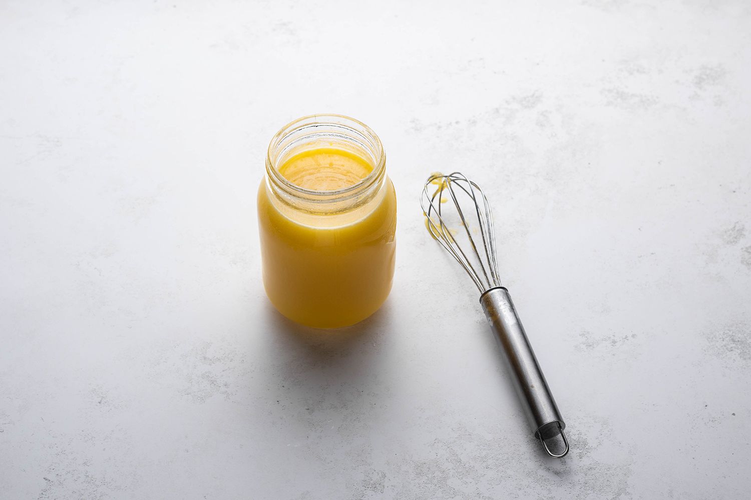 Lemon curd in a glass container, next to a whisk
