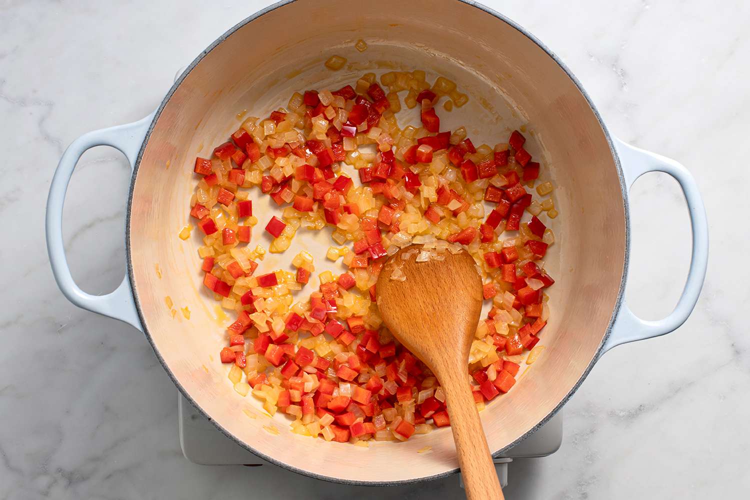 Onions and pepper in a pot on a burner, with a wooden spoon
