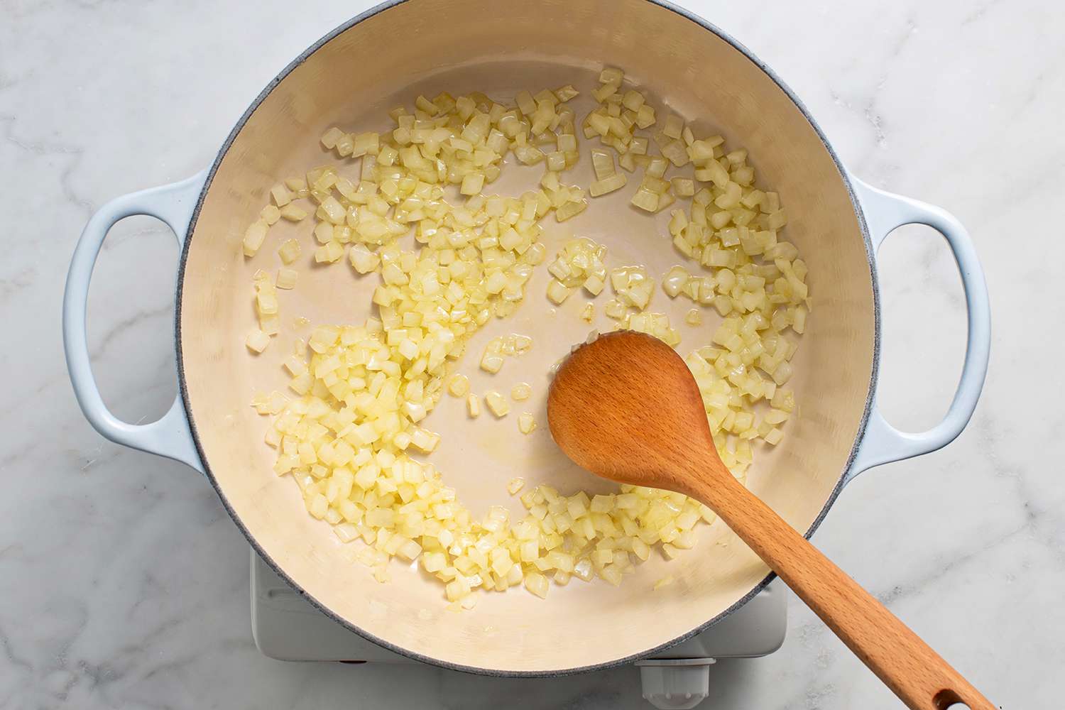 Onions cooking in a pot on a burner, with a wooden spoon