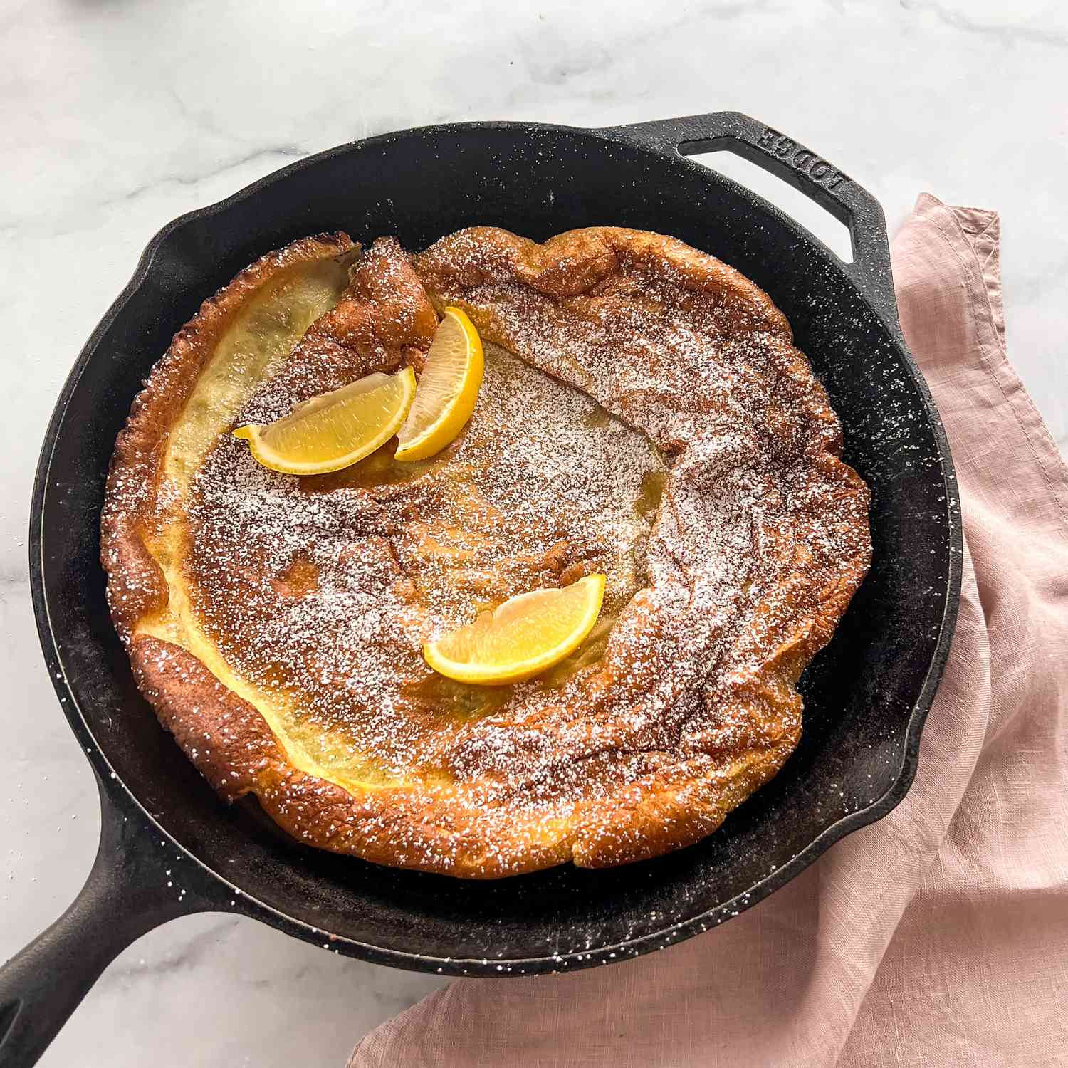 Golden brown Dutch baby in a cast-iron skillet with a few lemon wedges and powdered sugar