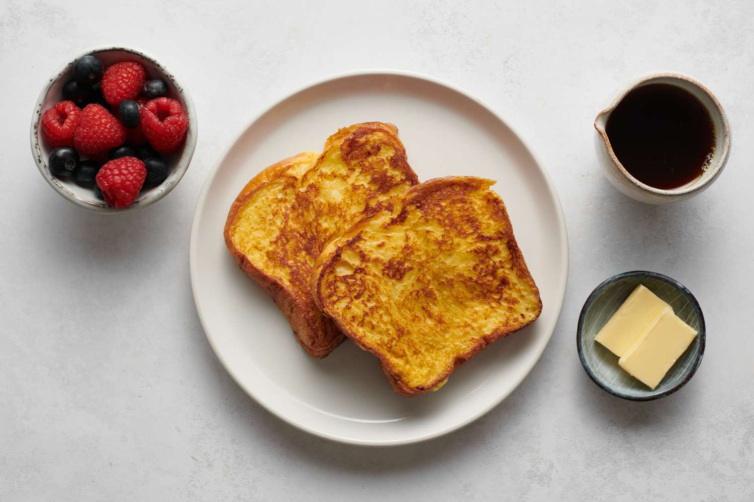 Um prato de torrada francesa servida com manteiga, xarope e frutas vermelhas