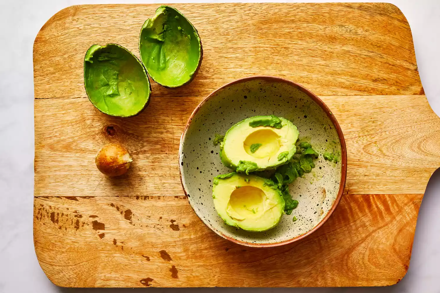 avocado peeled and seeded on cutting board resting in a bowl
