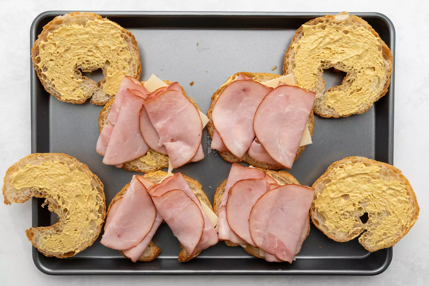 Metades de croissant cobertas com mostarda, queijo e presunto