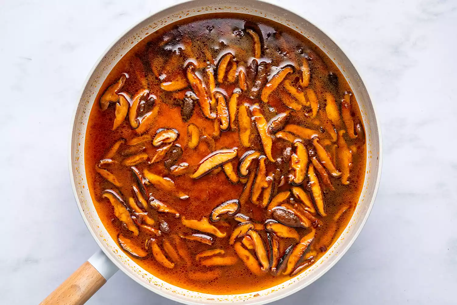 Uma frigideira com a água da massa reservada, cogumelos shiitake cozidos e chalotas