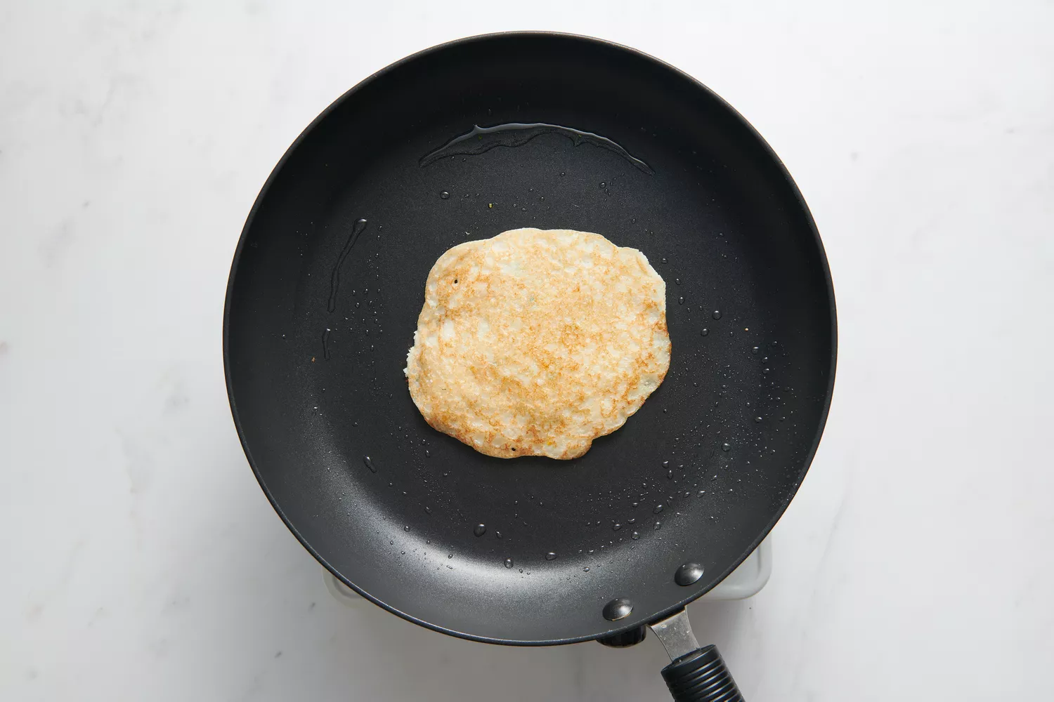 Uma frigideira untada com um uttapam dourado no centro, com a cebola-pimenta-coentro virada para baixo