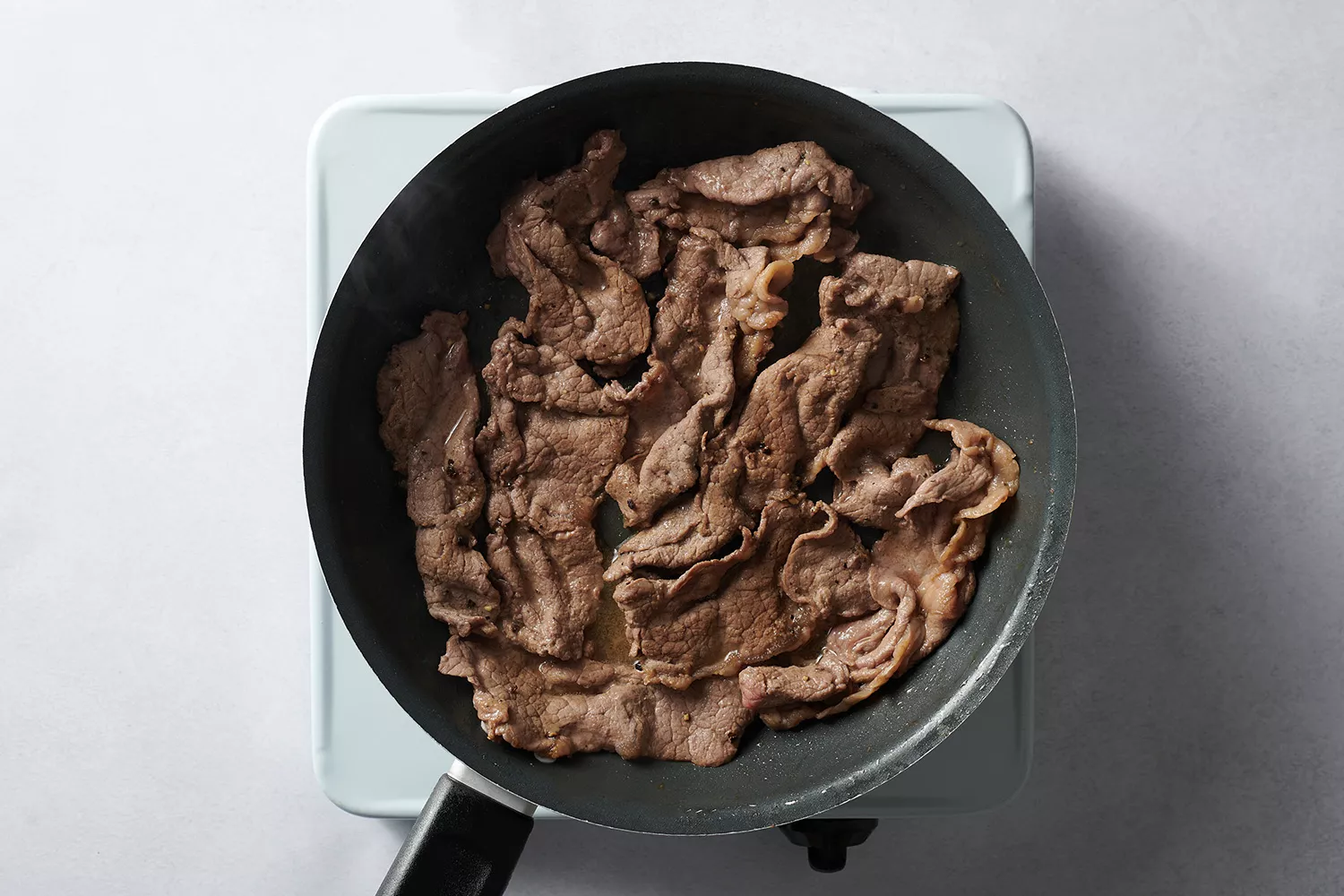 carne fatiada cozinhando na frigideira