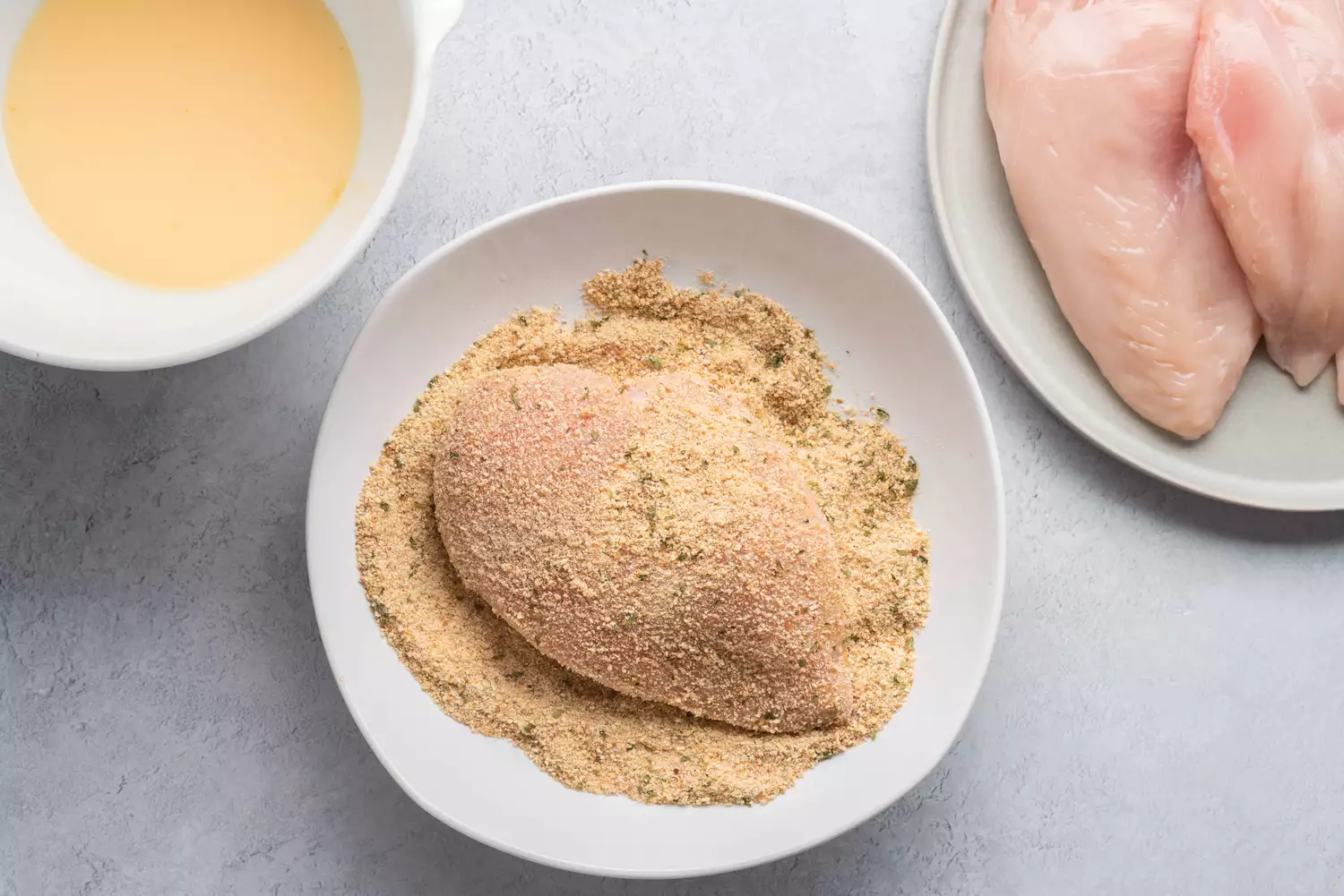 Peitos de frango achatados cobertos na mistura de leite e ovo e depois na farinha de rosca temperada