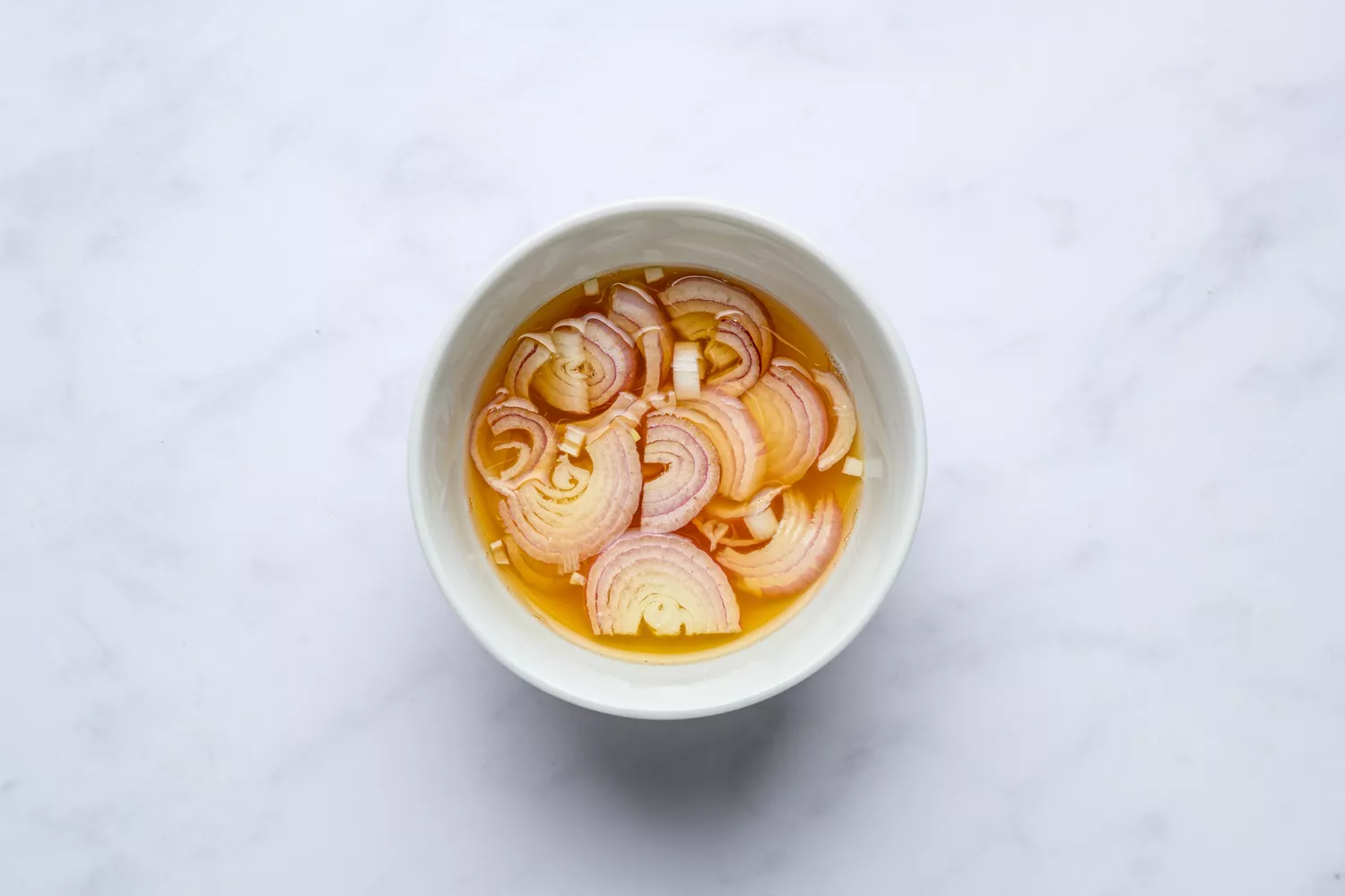 A bowl of sliced shallot with water, vinegar, honey, and salt