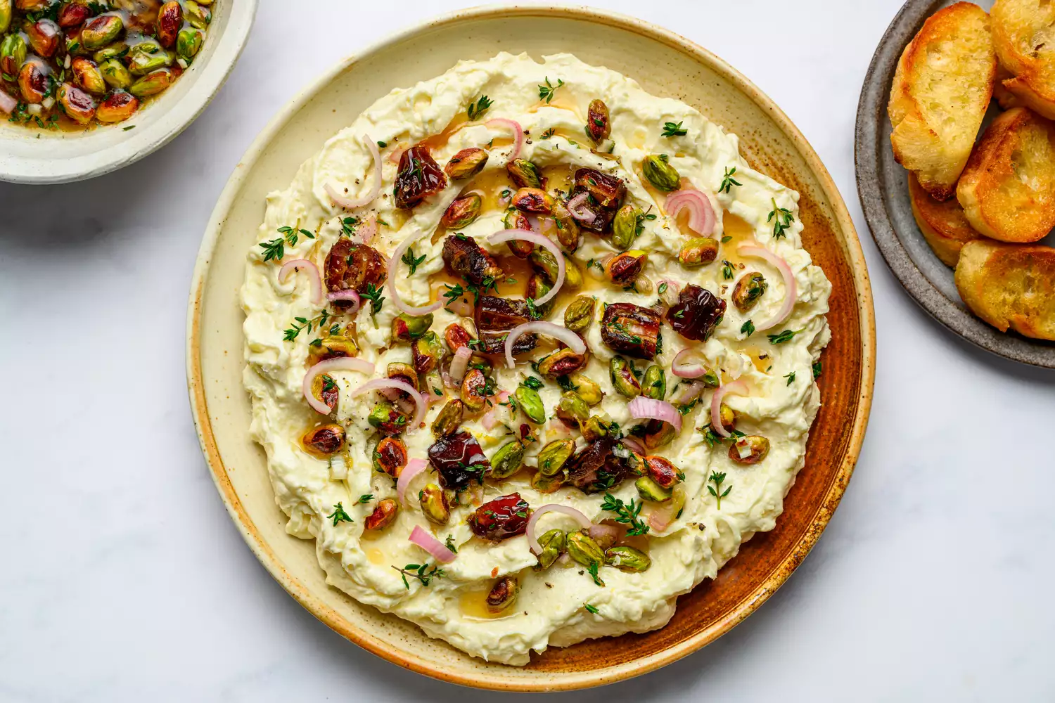 A platter of whipped brie topped with pickled shallots, fruit, and nuts