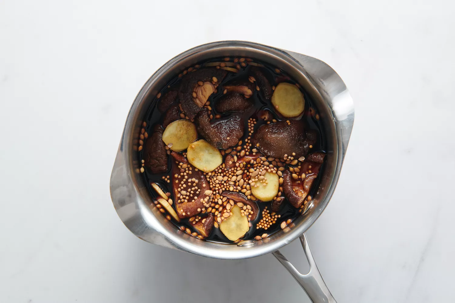 Uma panela com os cogumelos shiitake embebidos e picados, molho de soja, vinagre preto chinês, gengibre fatiado, sementes de mostarda, sementes de coentro e sal