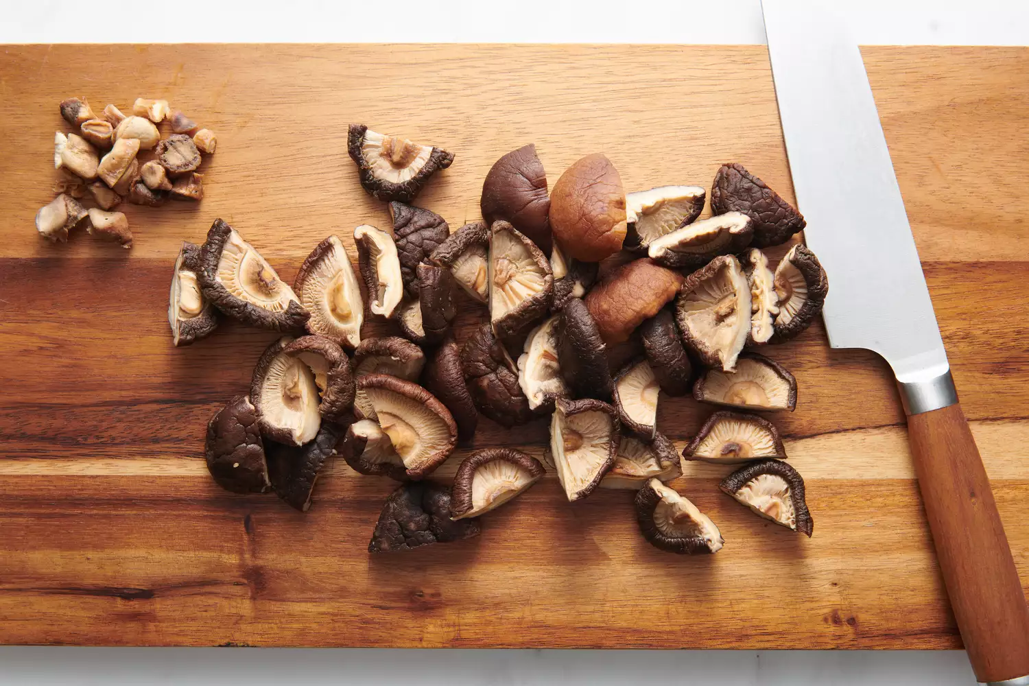 Uma tábua de corte com cogumelos shiitake embebidos com os talos aparados, cortados ao meio