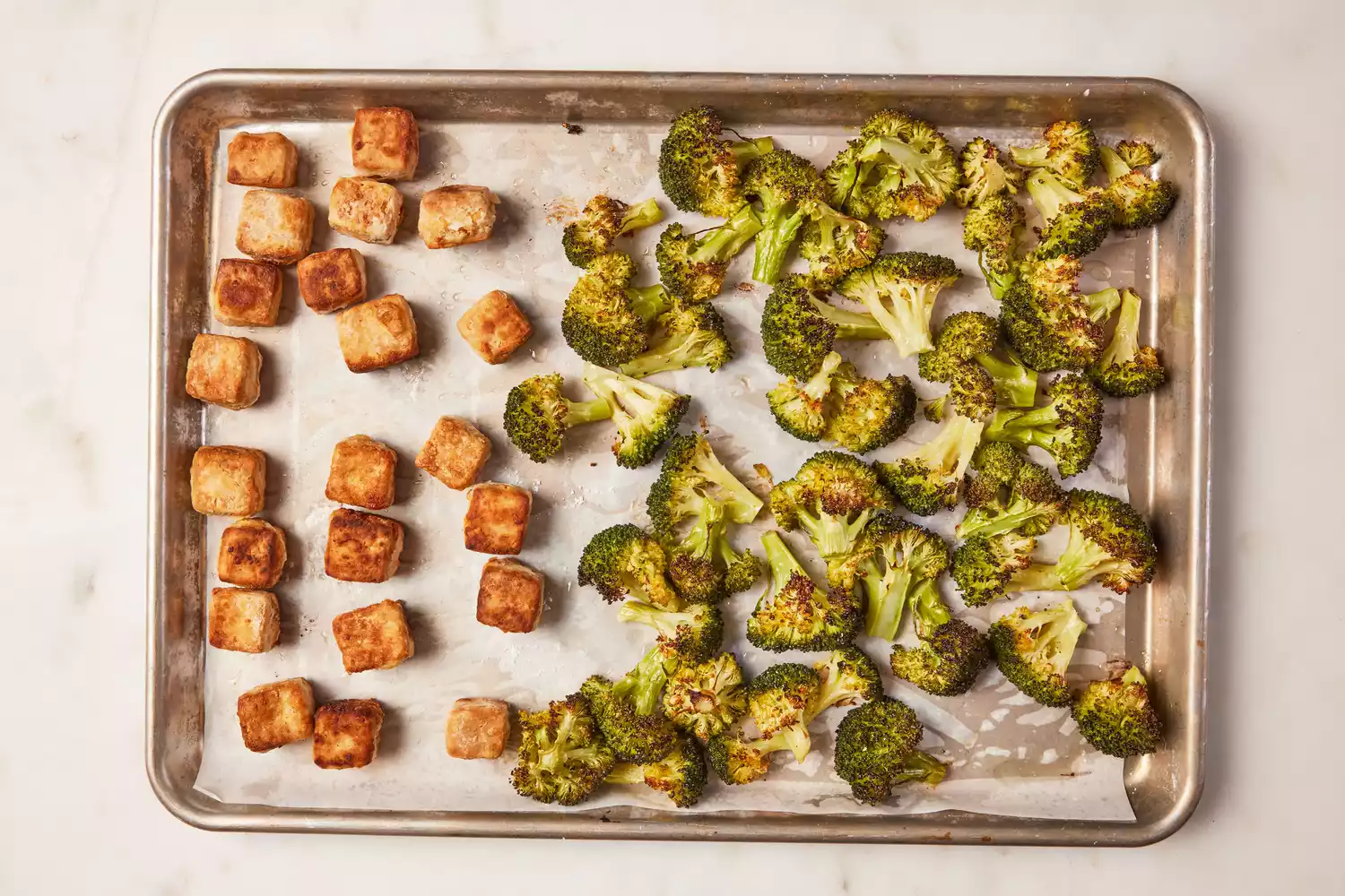 A parchment paper-lined baking sheet with crispy tofu and cooked broccoli florets