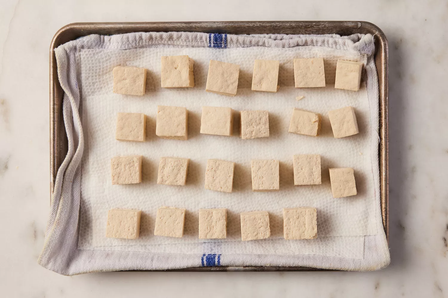 Cubed tofu draining on a baking sheet lined with kitchen towels