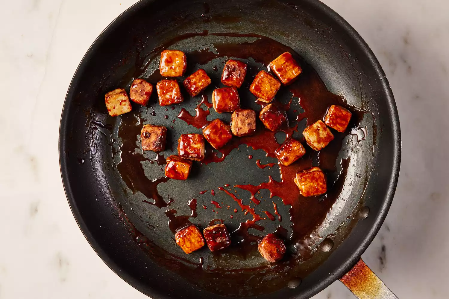 A nonstick pan of crispy tofu tossed in teriyaki sauce