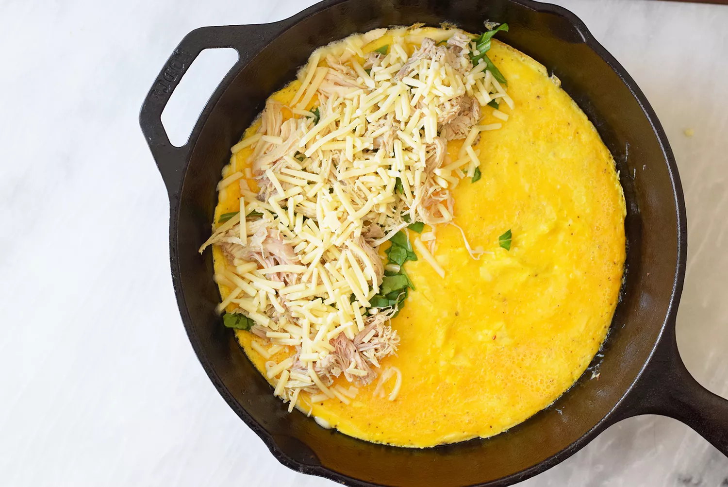 Queijo, frango e espinafre adicionados à frigideira com os ovos