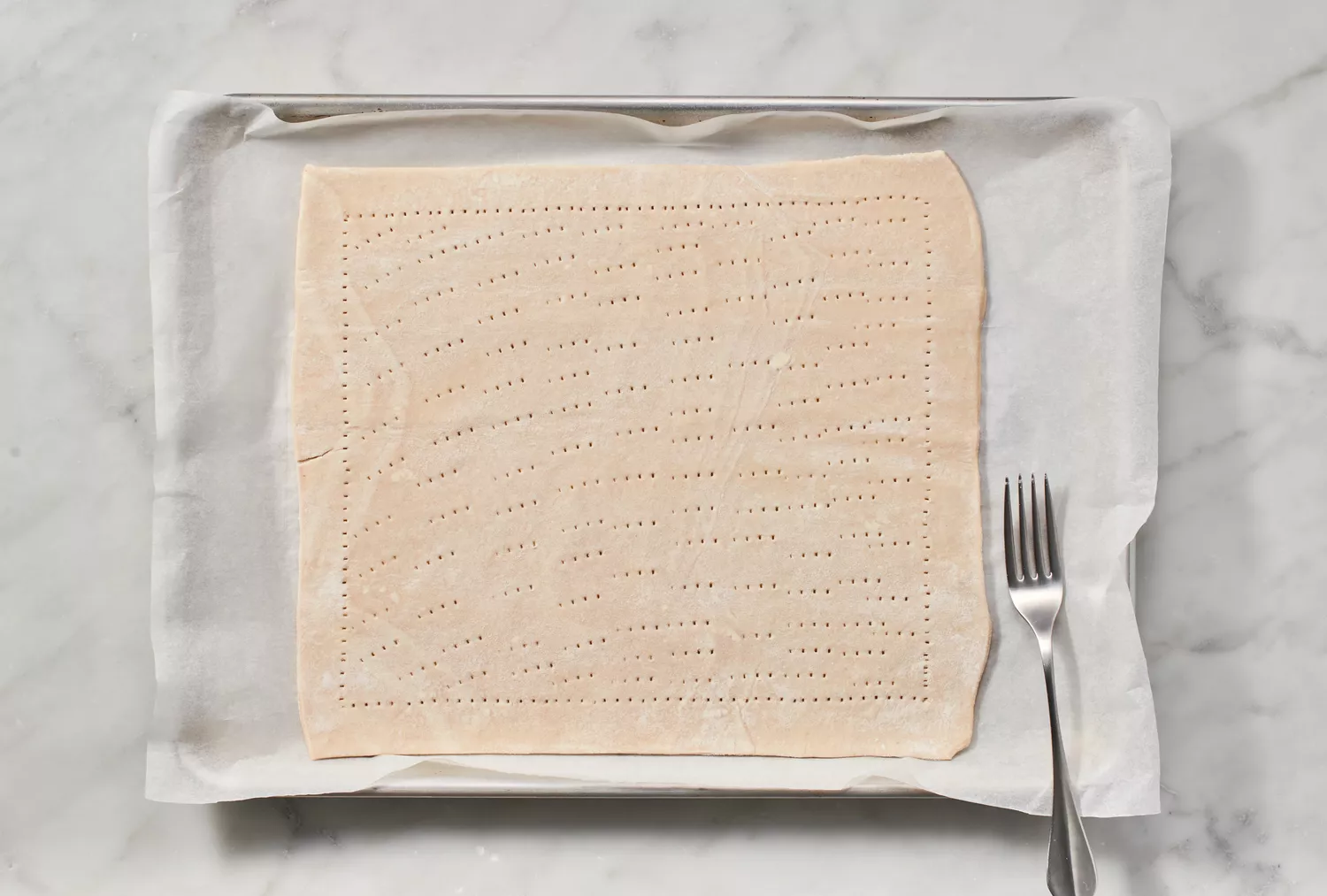 Uma peça retangular de massa folhada em uma assadeira forrada com papel manteiga