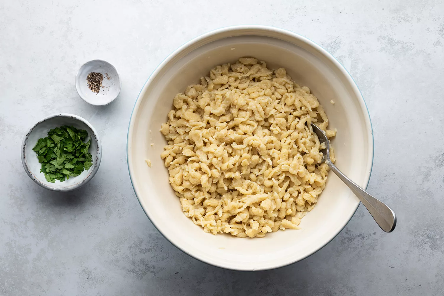 Spaetzle em uma tigela, ervas e pimenta do reino em pequenas tigelas