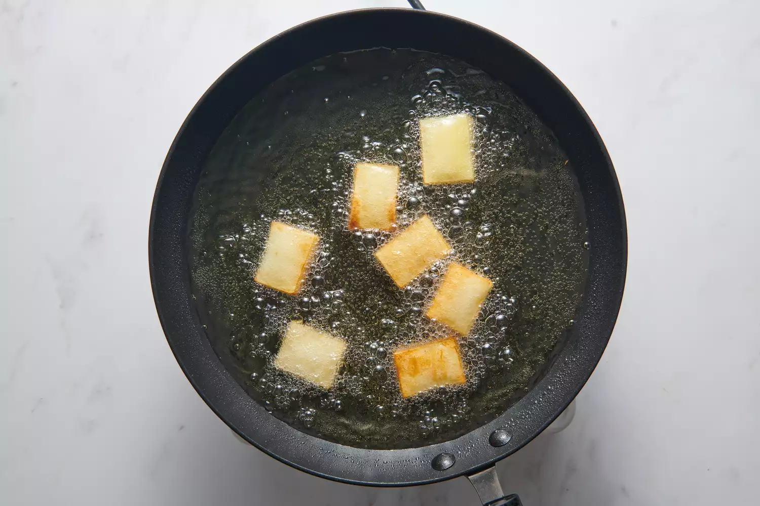 Uma panela com pequenas pilhas retangulares de batatas fatiadas fritando em óleo