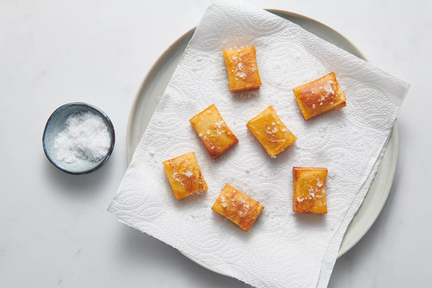 Um prato forrado com papel toalha com batatas em camadas milhões polvilhadas com sal em flocos