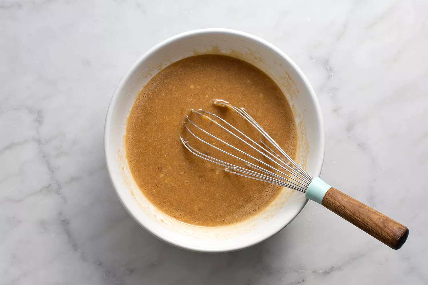 Bananas, leite, óleo de coco derretido, ovo, açúcar mascavo, açúcar granulado e baunilha em uma tigela com um batedor