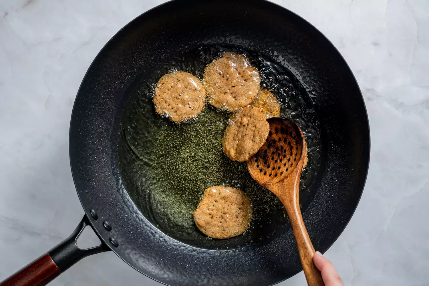 Uma colher de madeira virando um pedaço de mathri frito em um wok