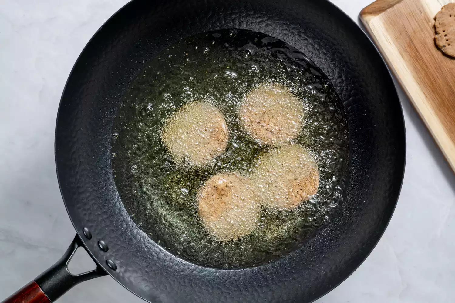 Um grande wok com quatro peças de massa de mathri fritando no óleo
