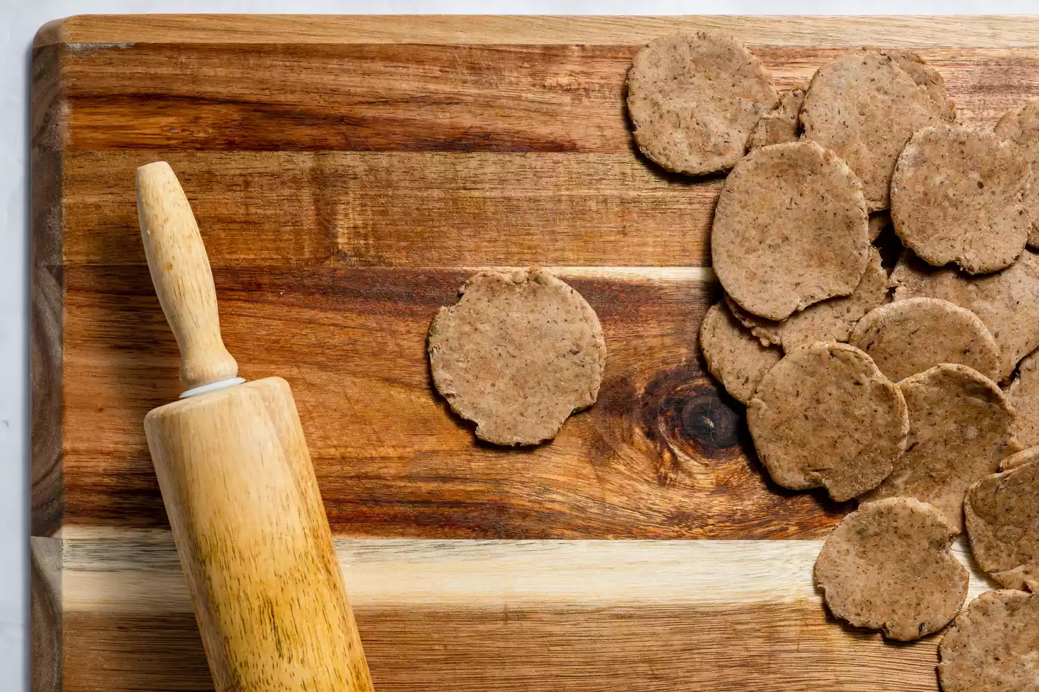 Uma tábua de corte com círculos flattenizados de massa de mathri com um rolo de massa