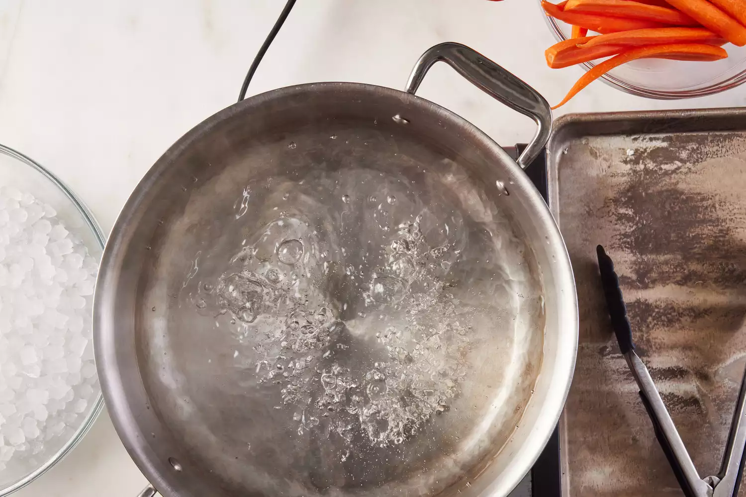 Uma panela grande de água fervendo, próxima a uma tigela de vidro cheia de gelo