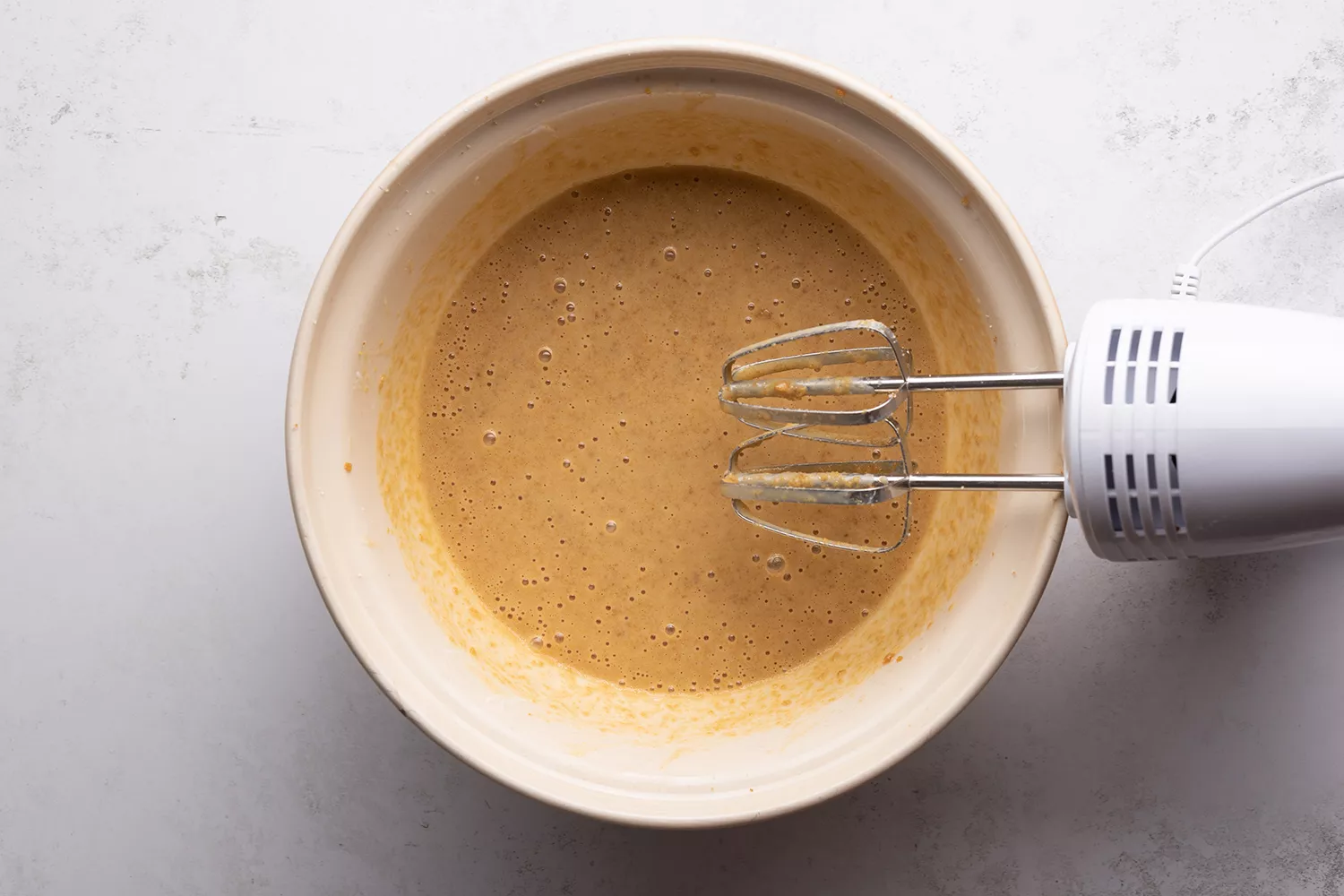 Iogurte e leite adicionados à tigela com a mistura de açúcar, ao lado de uma batedeira manual