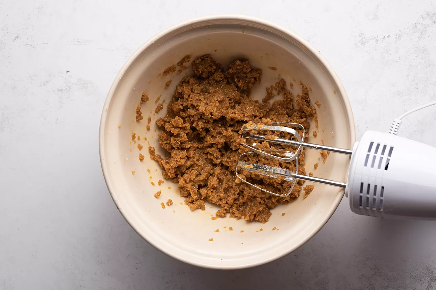 Baunilha e ovos adicionados à mistura de açúcar na tigela, ao lado de uma batedeira manual