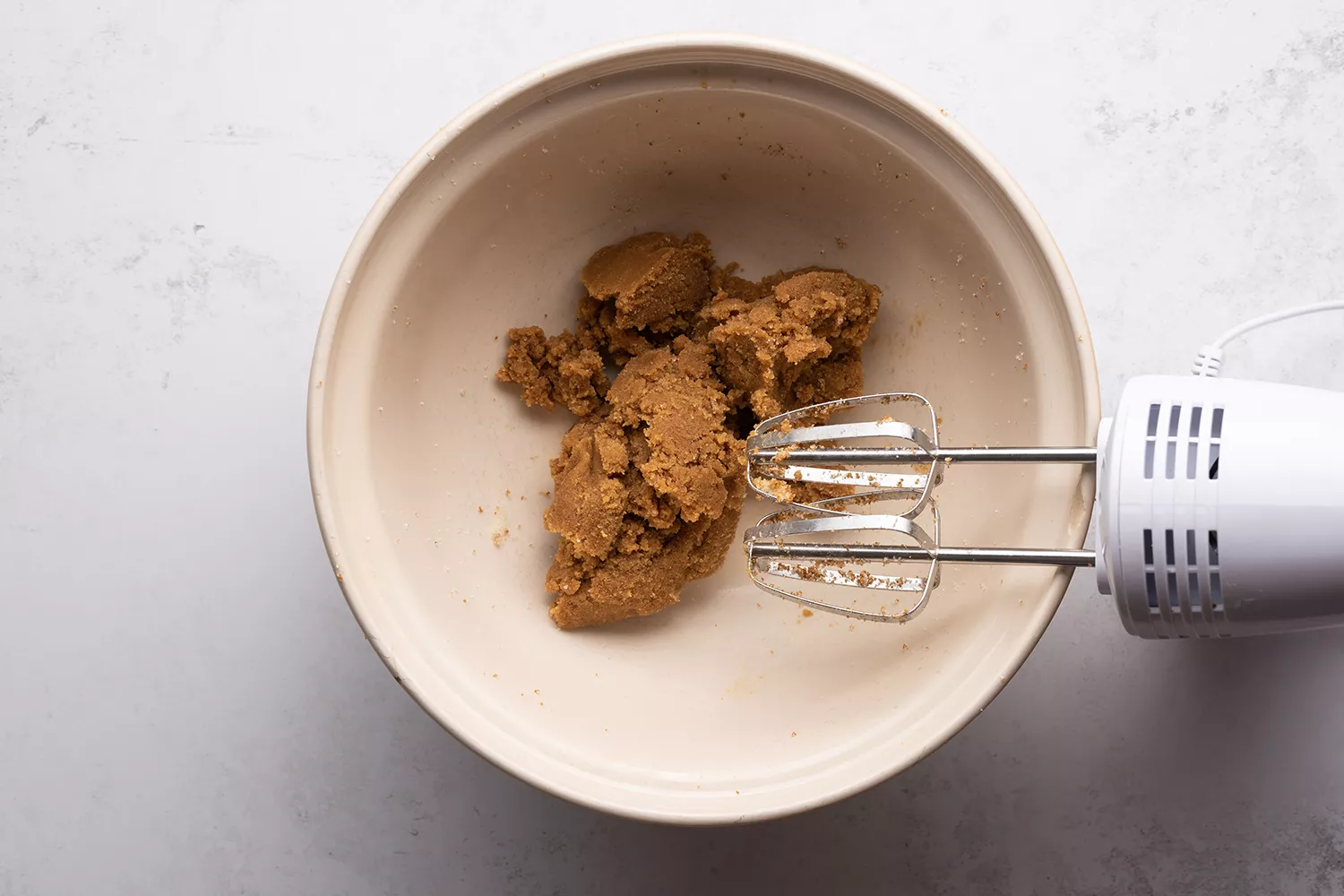 Açúcar granulado, açúcar mascavo e manteiga em uma tigela, e uma batedeira manual