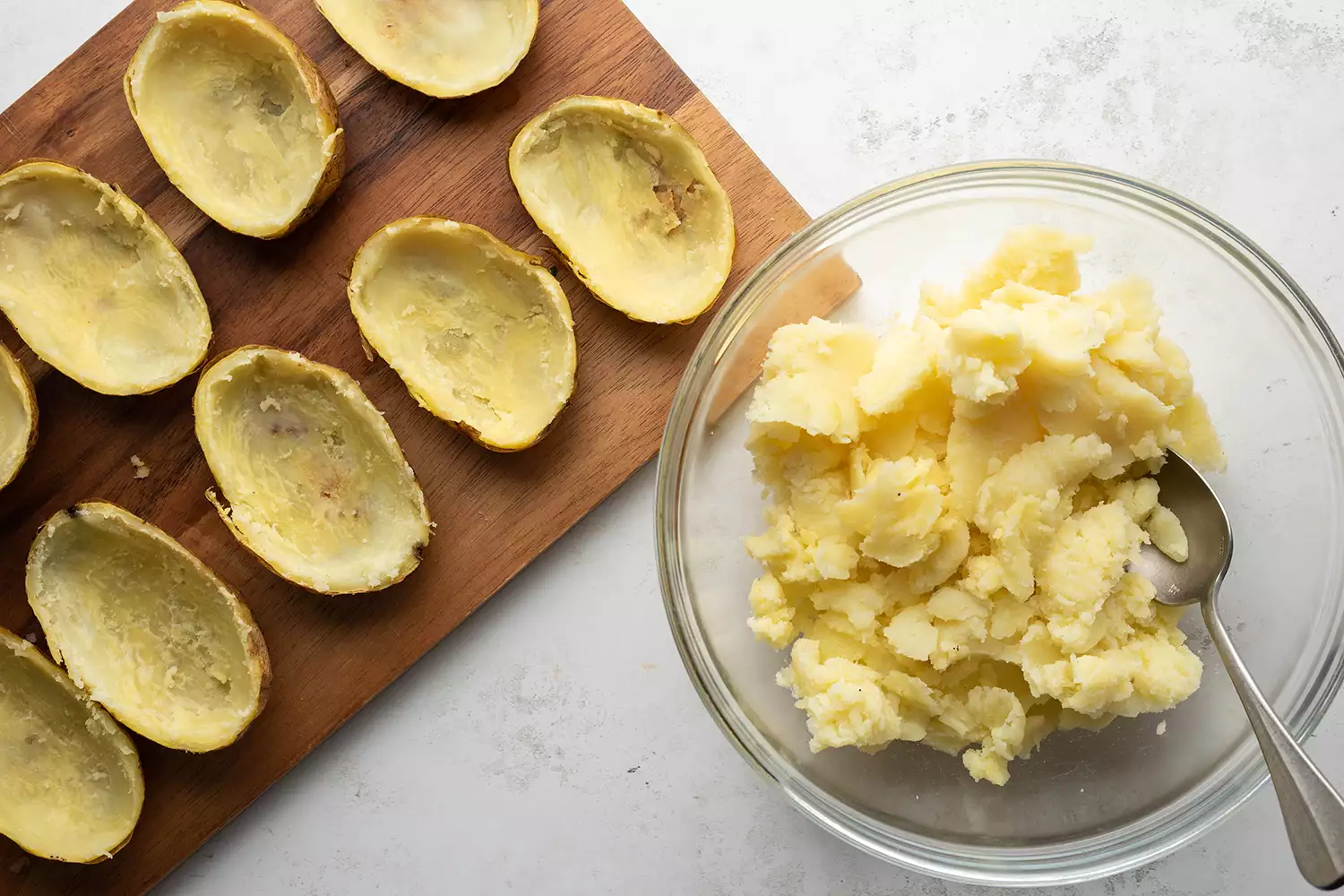 Flesh de batatas em uma tigela com uma colher, e cascas de batata em uma tábua de corte de madeira