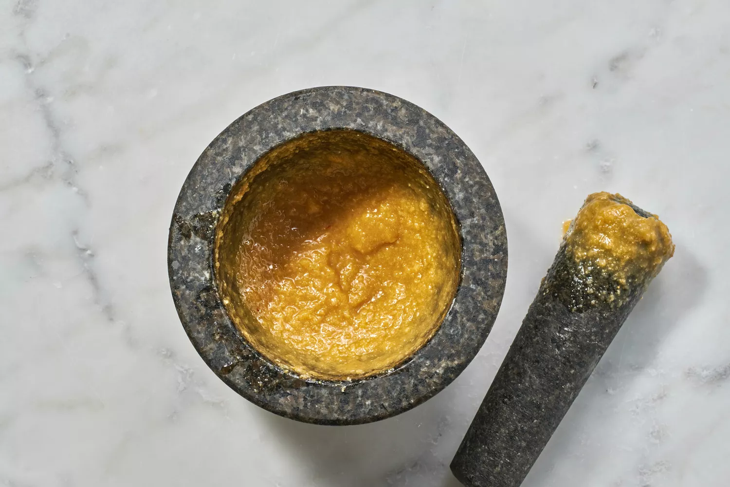 Um pilão e um pilão com uma pasta feita de alho, óleo de gergelim, sementes de gergelim torradas, caldo de galinha, açúcar mascavo, MSG e sal