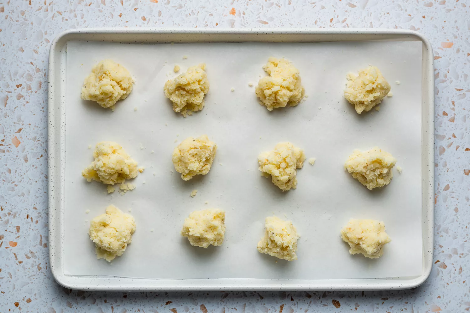 Uma assadeira forrada com papel manteiga com 12 porções iguais da mistura de laddu de coco