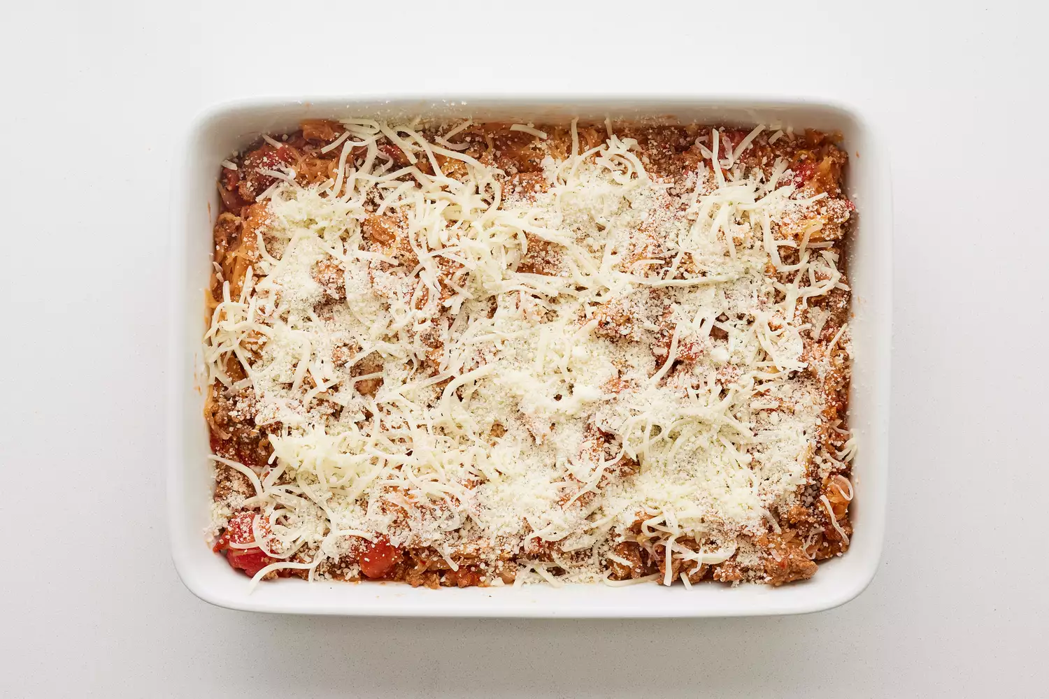 Uma assadeira com a mistura de abóbora espaguete e carne moída coberta com queijo parmesão e mozzarella ralados