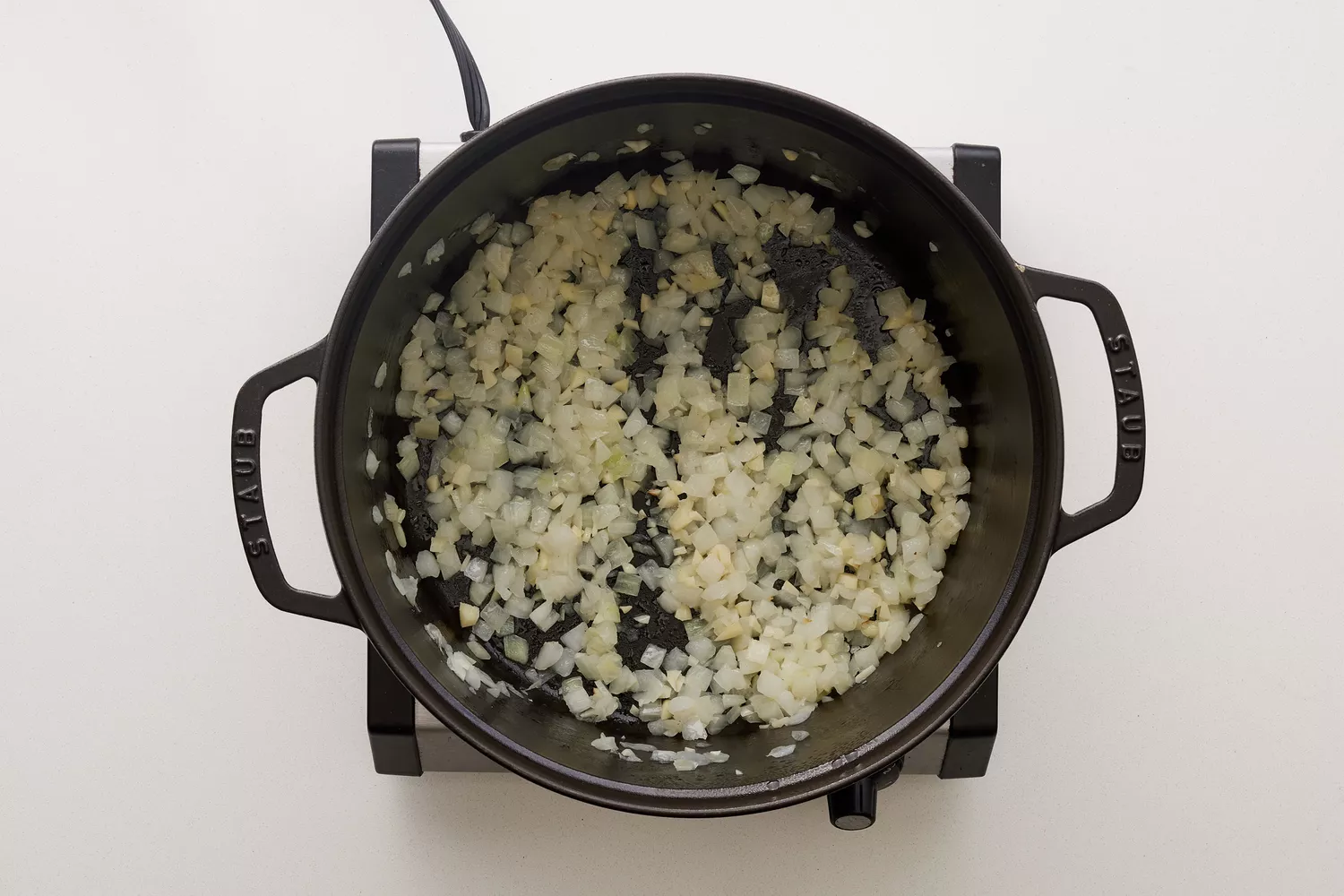 Uma panela de ferro com cebola e alho picados cozinhando em azeite