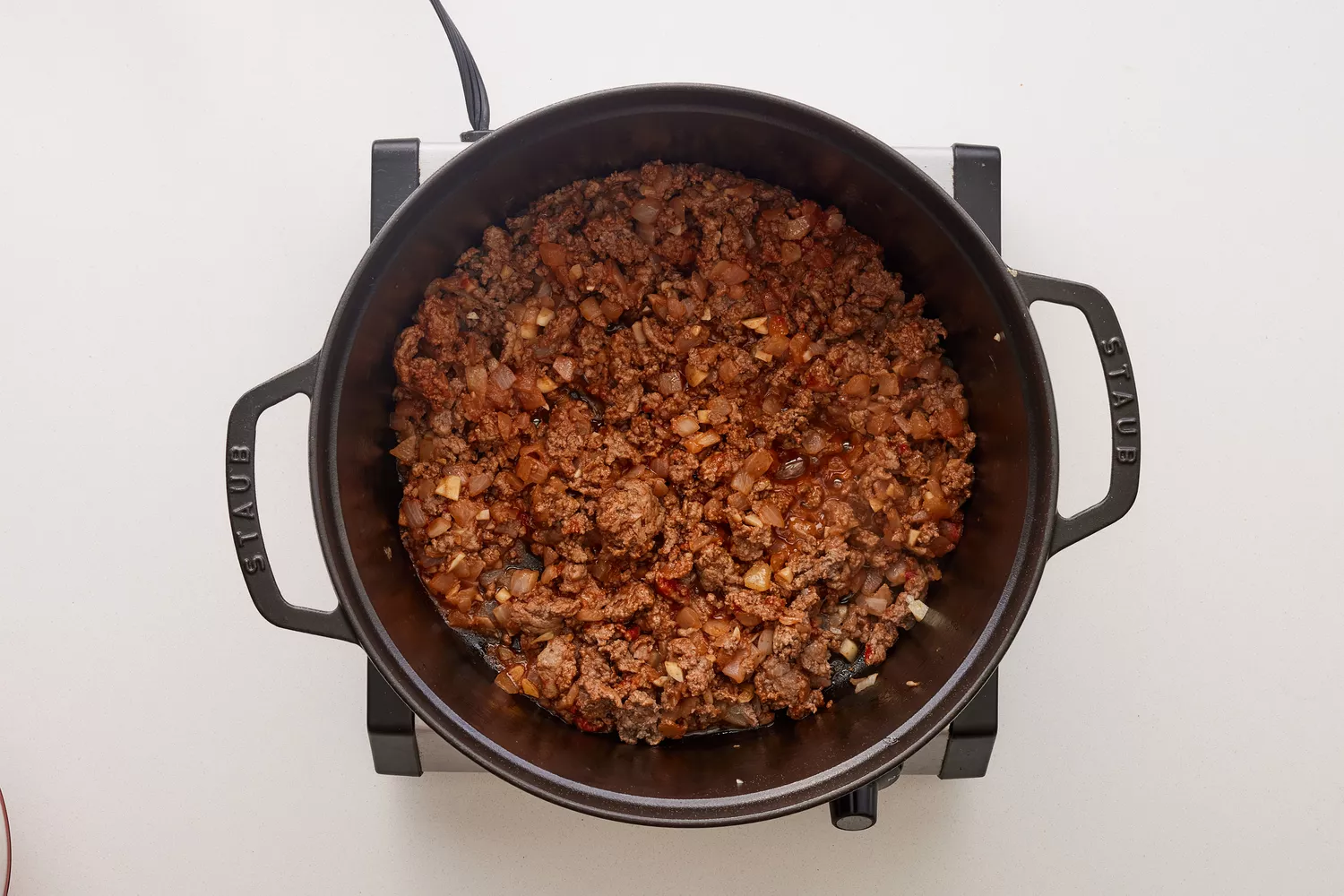 Uma panela de ferro com extrato de tomate, carne moída cozida, cebola picada e alho