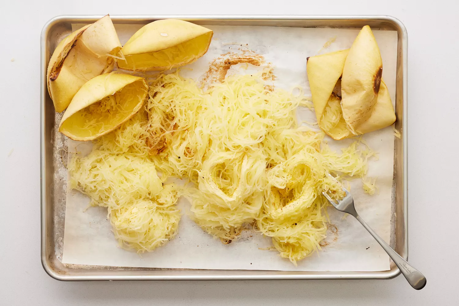 Uma assadeira forrada com papel manteiga com fios de abóbora espaguete desenhados com um garfo