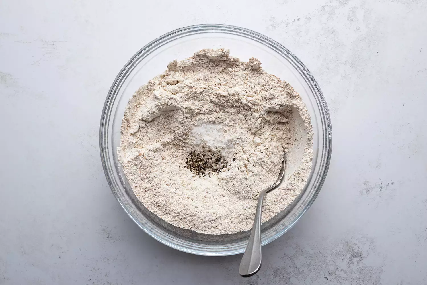 Farinha, sal e pimenta em uma tigela de vidro com uma colher
