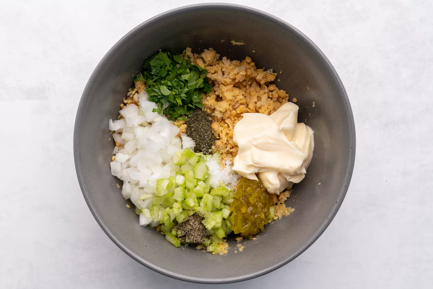 Vegetais, maionese e temperos adicionados ao grão-de-bico amassado na tigela