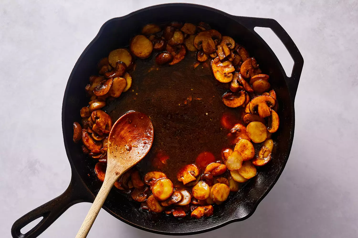 Castanhas de água, cogumelos e molho em uma frigideira de ferro fundido, com uma colher de madeira