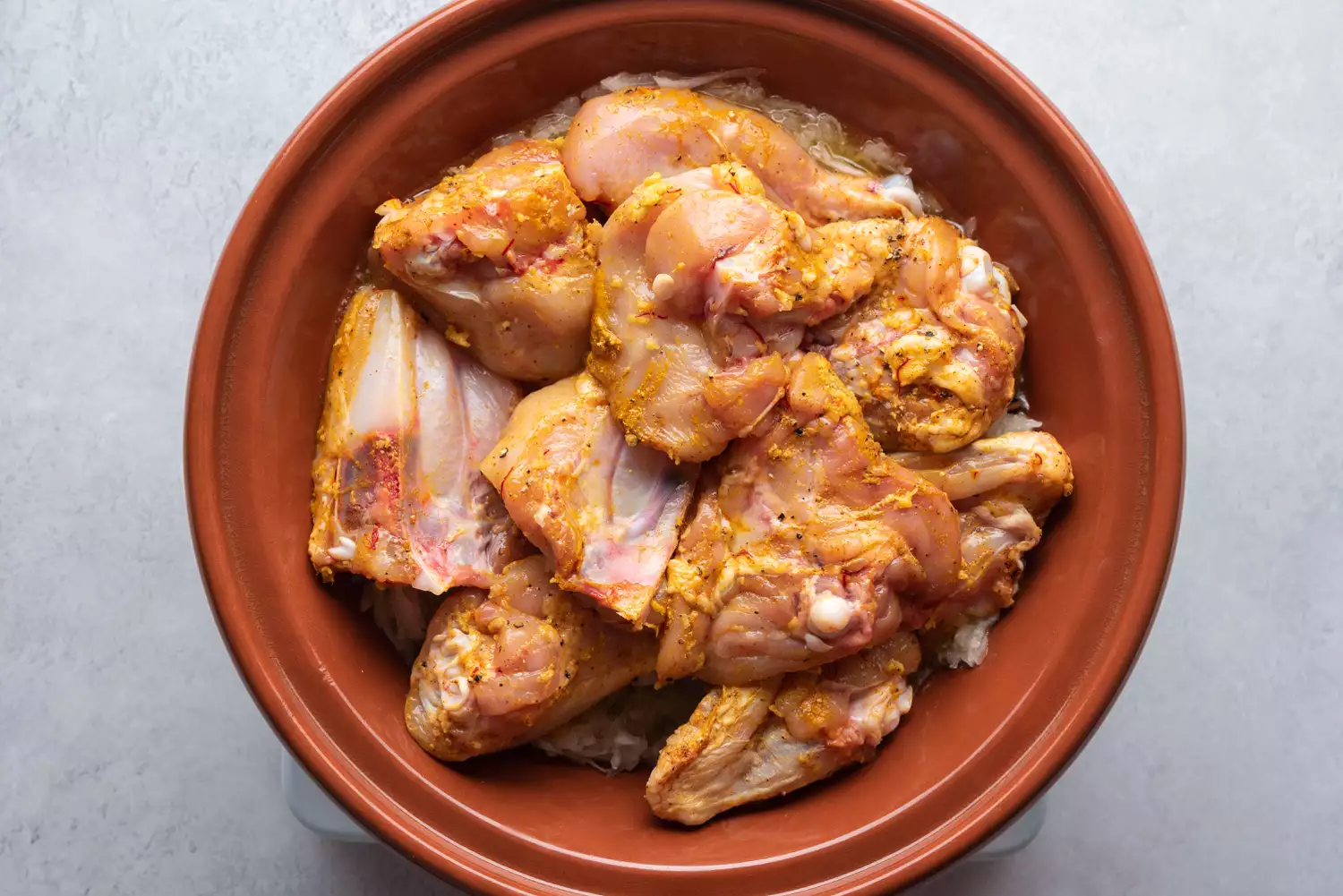 frango cru marinado no tagine sobre a mistura de cebola