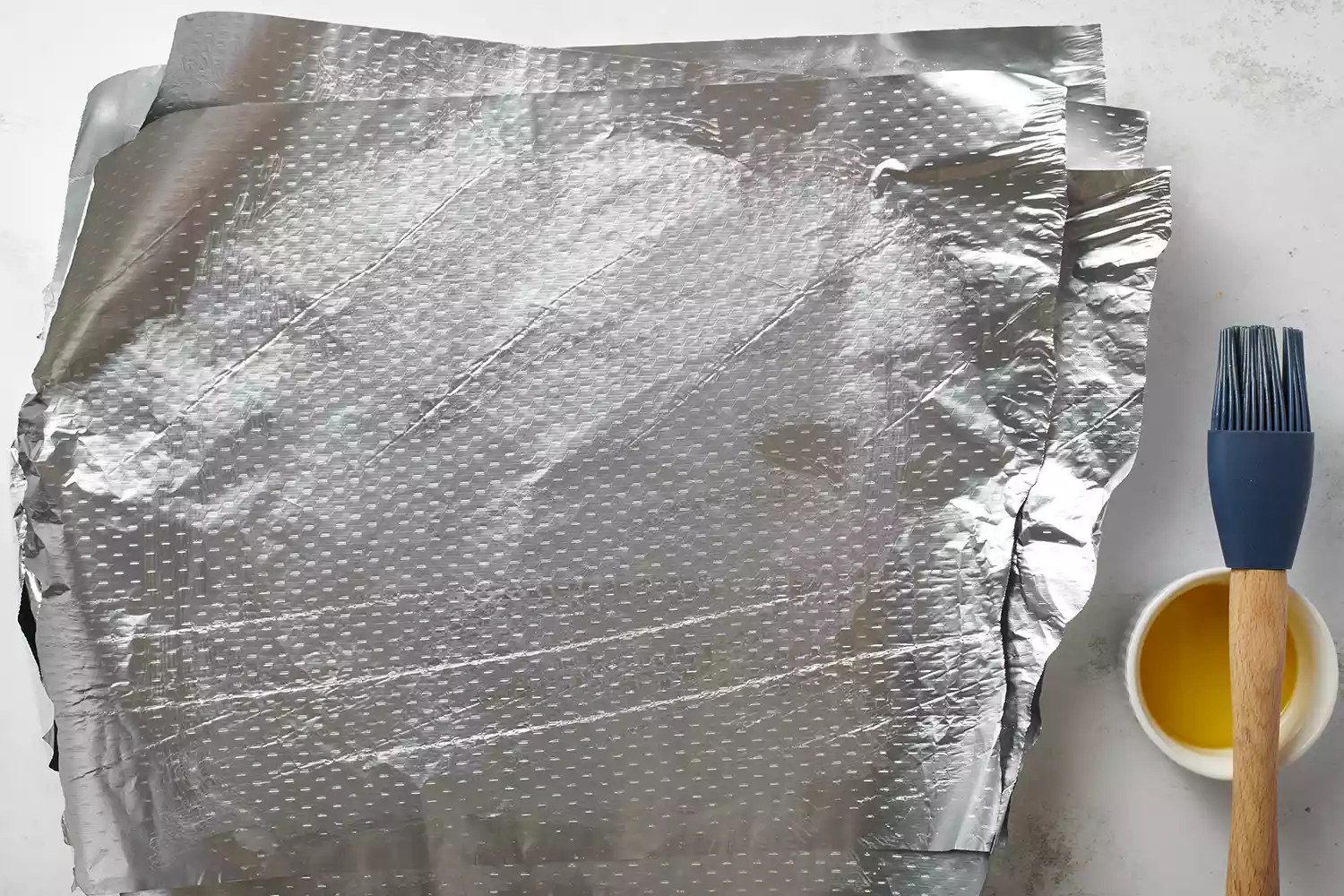 folhas de papel alumínio e uma tigela de óleo sobre uma superfície de mesa