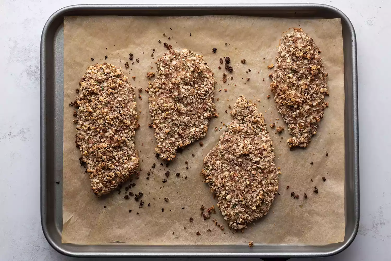 Frango assado coberto de amêndoa em uma assadeira forrada com papel manteiga